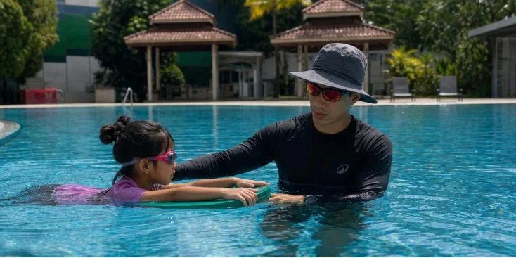 Coach Gary supporting a young swimmer on a kickboard in the pool